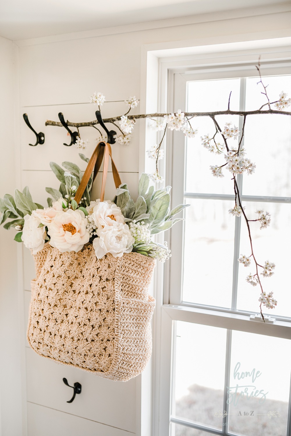 A crochet tote bag hanging on a hook with flowers inside